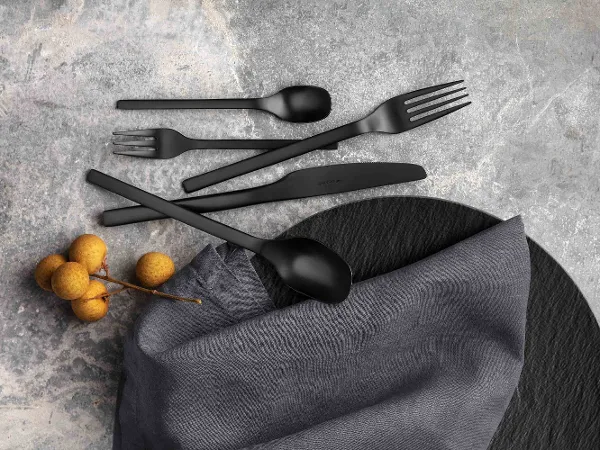 Black Manufacture cutlery set with a fabric napkin and decorative berries on a textured grey surface.