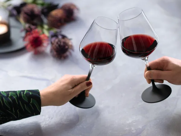 Manufacture red wine glasses in black with red wine Two people clinking two filled Manufacture red wine glasses with black stems from Villeroy & Boch.