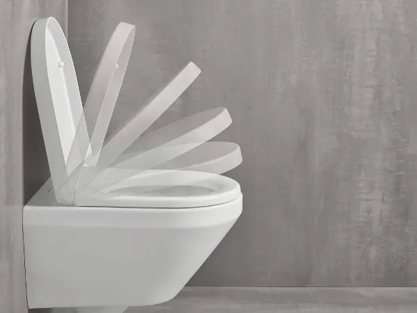 Un WC sospeso con coperchio aperto in varie fasi di chiusura su uno sfondo grigio semplice.