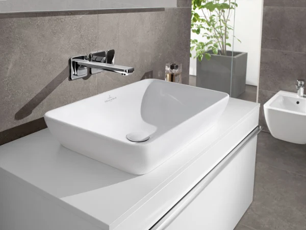Rectangular white Venticello washbasin Modern bathroom washbasin with a rectangular white basin, a wall-mounted tap and a small plant in the background.