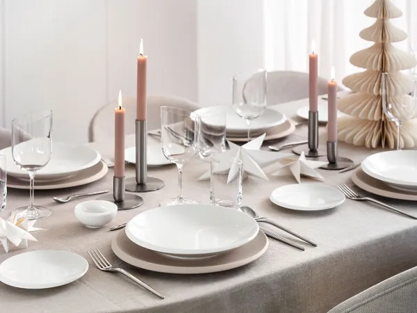 Top-down view of a modern, festive table setting featuring Villeroy & Boch’s NewMoon Beige collection: flat bowl, dinner and bread plates, paired with NewMoon cutlery, wine glasses and tumblers. Soft Christmas décor accents—such as light-toned ornaments, pine branches or candles—add a refined seasonal touch to the calm, natural tones and minimalist forms.