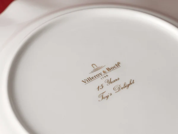 The underside of a white Villeroy & Boch plate with gold lettering and the inscription "15 Years Toy's Delight." 