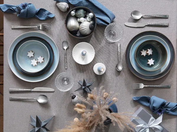 Table decoration with Crafted plates, silver cutlery, star-shaped decorations and dried flowers on a wooden table.