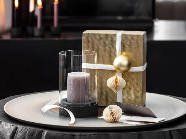 A Manufacture hurricane lamp with a candle A Manufacture hurricane lamp with a candle next to a gift wrapped with a white box and ornaments.
