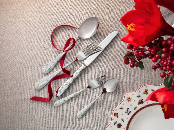 A Toy's Delight cutlery set, consisting of a spoon, fork, knife and two small spoons, arranged on a beige cloth with a red bow.