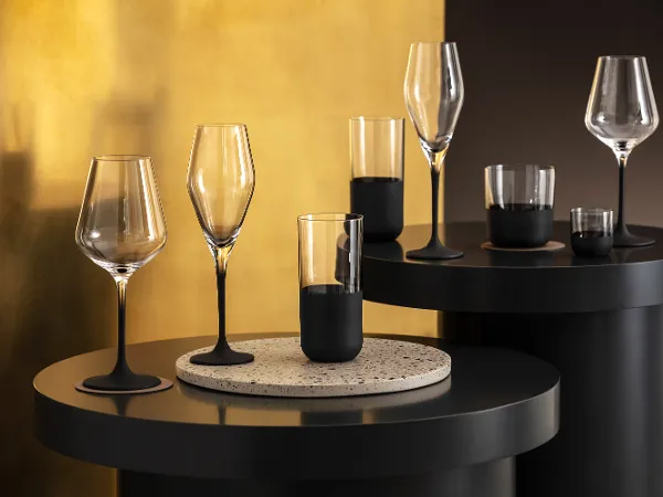 Several elegant Manufacture glasses on modern black tables against a textured gold background.