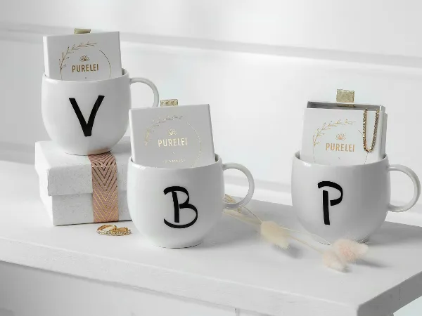 Three personalized Letters mugs with monogram letters "v," "b" and "p" filled with jewelry and boxes of cosmetic products on a white shelf.