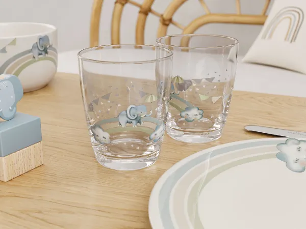 Two empty Boho Kids Walk like an Elephant decorated glasses on a table with matching plates and a napkin holder.