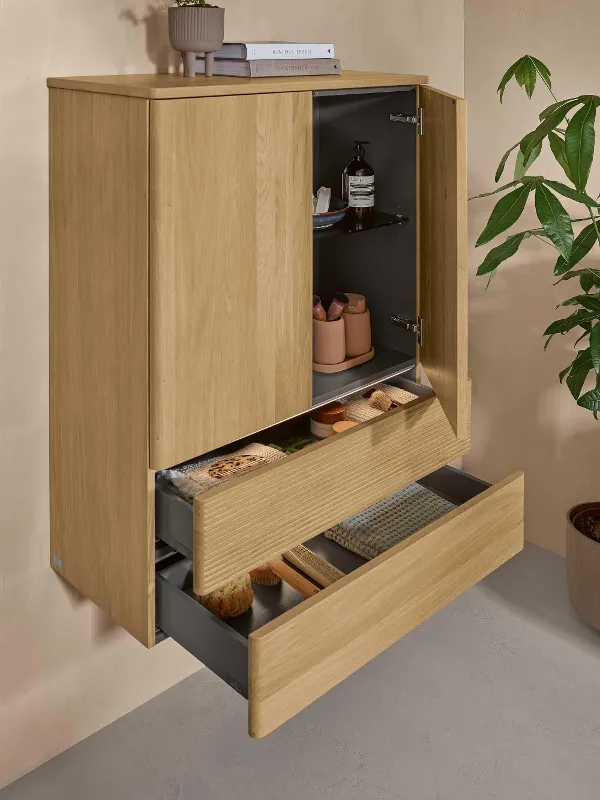 A Villeroy & Boch bathroom cabinet in light-coloured wood with two doors and two open drawers on a natural wall.