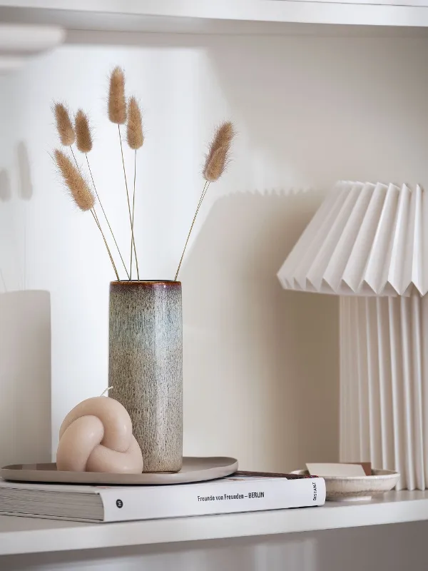 A shelf with a tall beige Lave vase and a lamp on top.