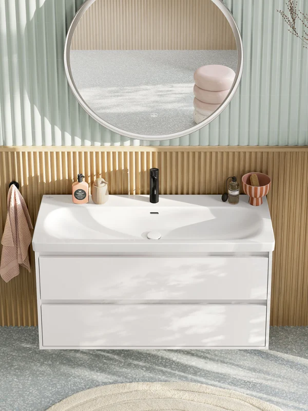 Ruime, moderne wastafel met de Villeroy & Boch Skyla collectie. Ruime, moderne wastafel in pastelkleuren van bovenaf gezien, bestaande uit een wastafel met witte onderkast, een ronde verlichte spiegel, een zijkast en een zwarte kraan uit de Skyla badkamercollectie.