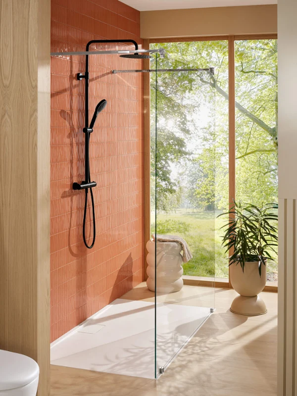 Verve Showers fitting with Architectura shower tray in a bright bathroom Modern shower with glass walls and black fittings next to a large window overlooking greenery.