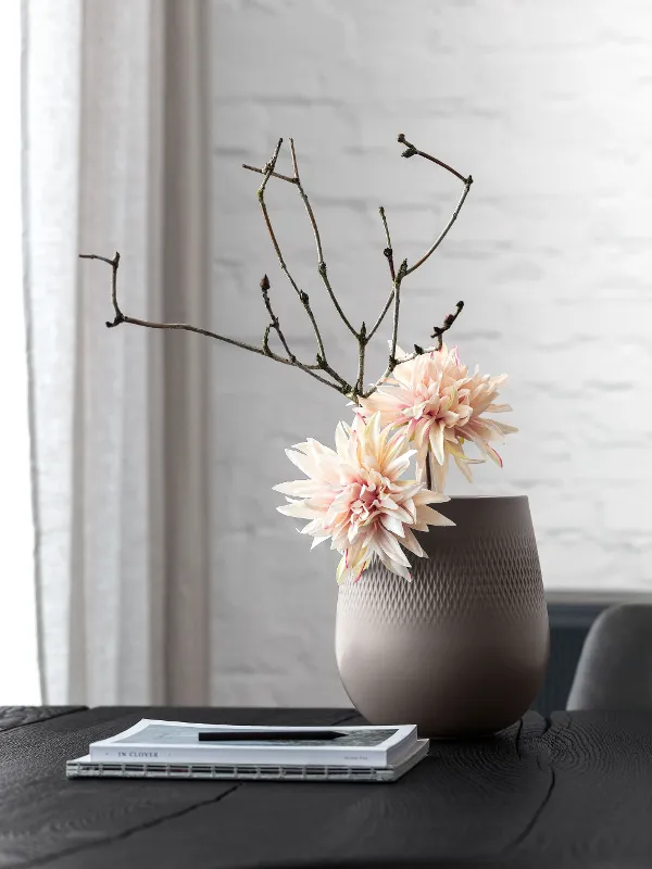 A large Manufacture vase with a subtle flower arrangement on a table.