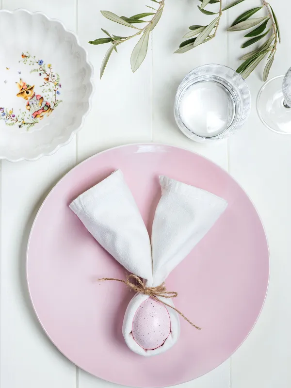 A Villeroy & Boch pink Rose Garden plate decorated with an egg wrapped in a white napkin that looks like a bunny and tied together with string.