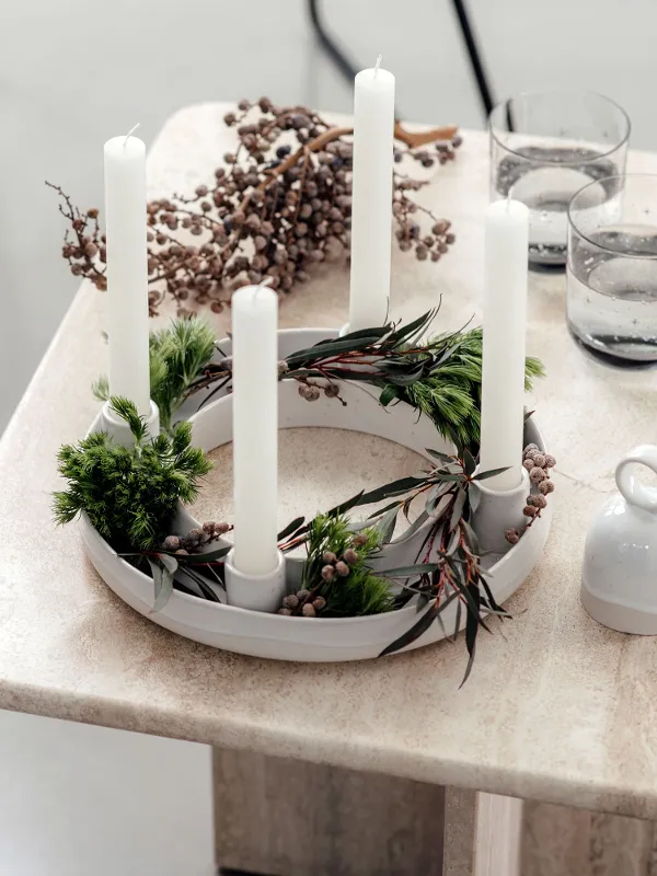 A beige table with a Winter Glow Advent wreath in the centre, surrounded by Winter Glow glasses and a magazine.