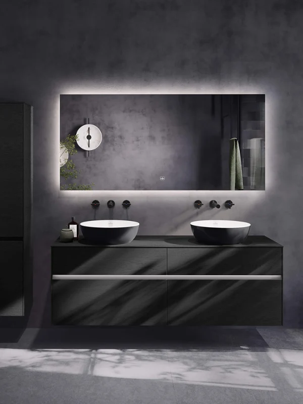 Czarna łazienka z dwukolorową umywalką nablatową: Czarna łazienka z dwukolorową umywalką nablatową Nowoczesna łazienka z podwójną umywalką, dużym podświetlanym lustrem, czarnymi szafkami i minimalistyczną armaturą na tle szarych ścian.