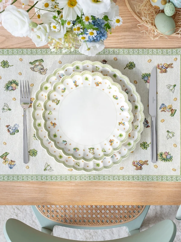 Table setting with stacked Easter Delight plates on a placemat, napkin with ring, and flowers, viewed from above.