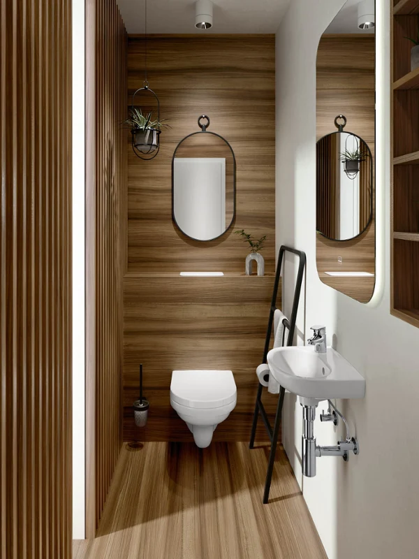 Moderno cuarto de baño con paneles de madera, inodoro suspendido con espejo ovalado, un pequeño lavabo blanco con espejo grande y un estante con utensilios. A la derecha hay una escalera con un marco negro para decorar y guardar cosas.