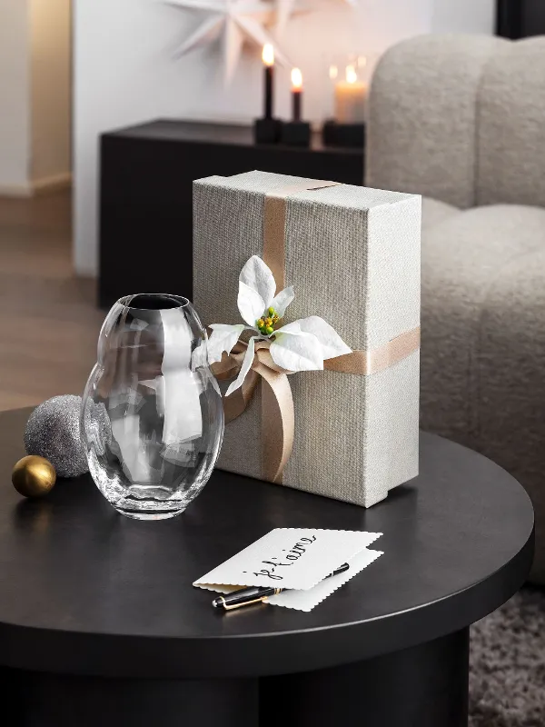 A table with a wrapped gift box and a decorative Rose Garden Home glass vase A table with a wrapped gift box, decorated with a white bow and a decorative Rose Garden Home glass vase