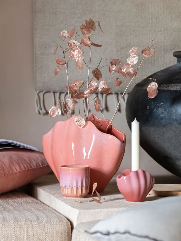 A table with a pink Perlemor decoration vase beside a candle.