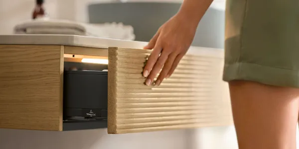 Antao minimalist console for the bathroom A woman in a bathroom opening a console drawer in the Antao bathroom furniture collection by Villeroy & Boch.
