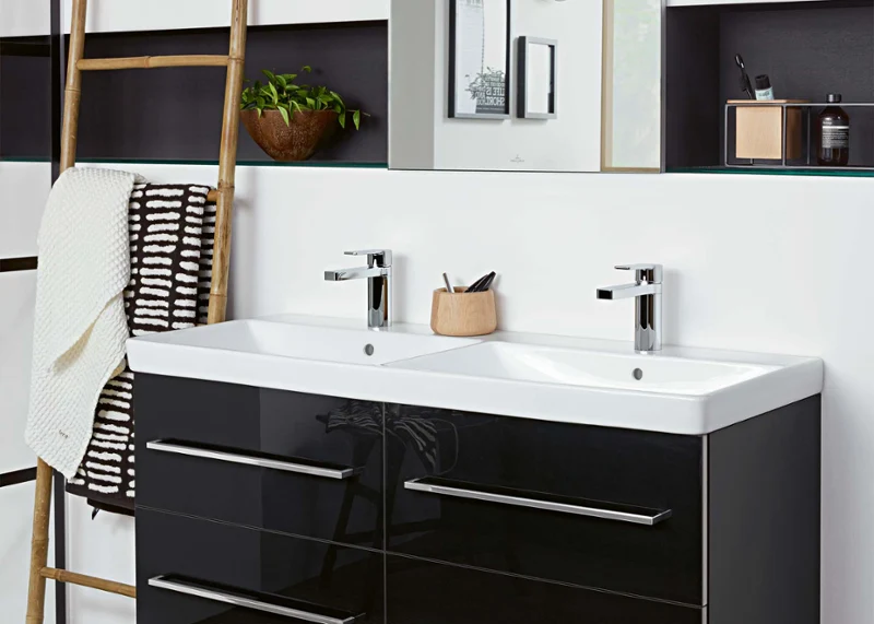 Avento double washbasin with black drawers and a mirror Modern bathroom with an Avento double washbasin with black drawers, a large mirror, a wooden ladder with a white towel, a plant and a clock on the wall.