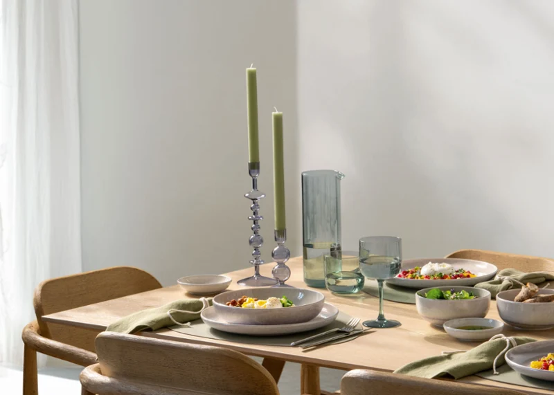 Una mesa de madera con vajilla Perlemor y candelabros Like Home Una mesa de comedor de madera con platos llenos de comida, vasos, velas verdes y vajilla minimalista.