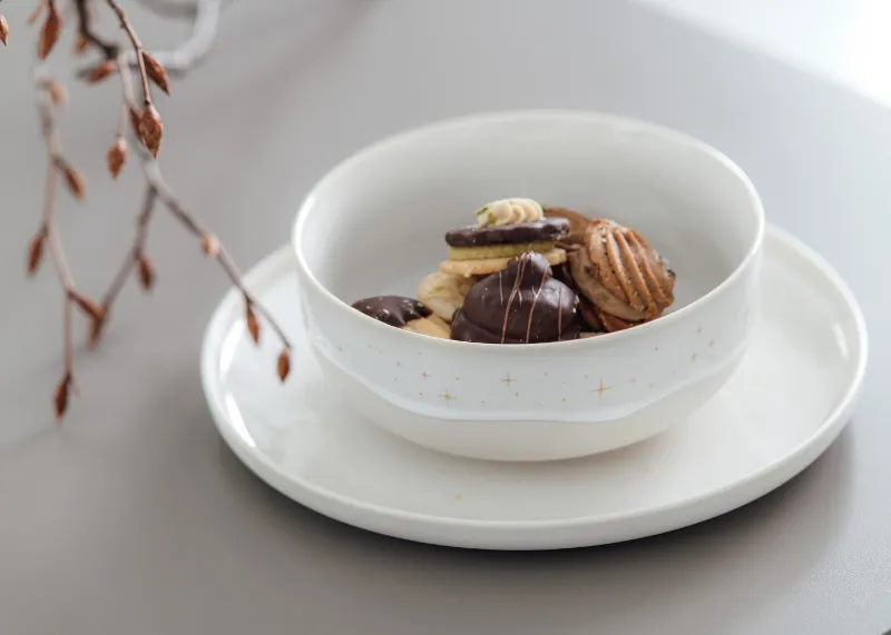 A Winter Glow bowl with various biscuits on a Winter Glow plate with decorative twigs in the background.