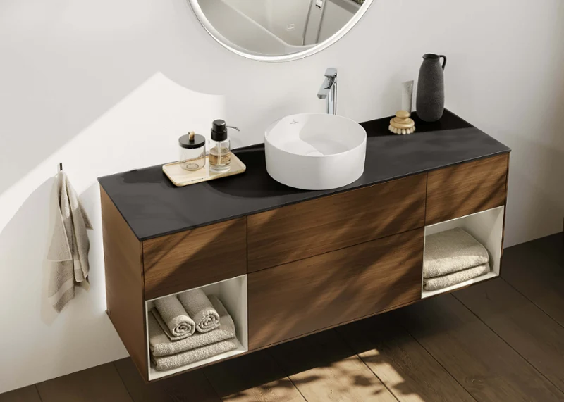 Wooden vanity with round white basin Finion furniture vanity in warm wood with black countertop, round white basin and open shelves for towels, combining elegance and function.