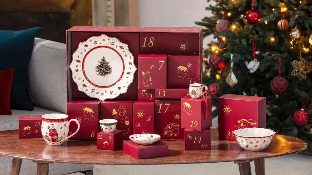 Red Advent calendar boxes and Christmas dishes are placed on a wooden table next to a decorated Christmas tree.