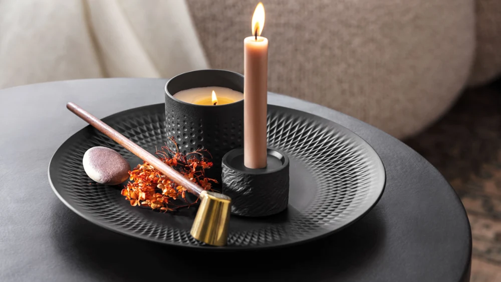 Een brandende kaars met wierook en gedroogde bloemen op een decoratief zwart bord van Manufacture.