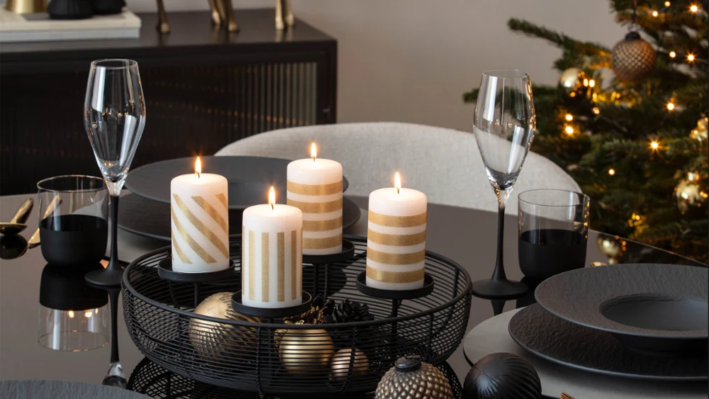 En una mesa de comedor decorada para la ocasión, con platos, vasos y adornos festivos, arden cuatro velas rayadas.