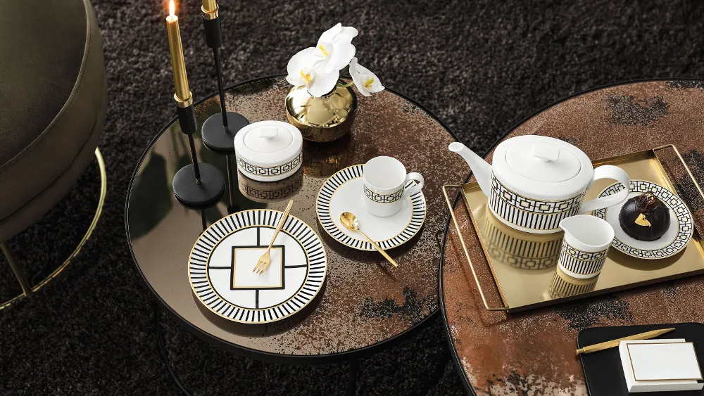 MetroChic tea service on a round table with golden accents, accompanied by orchids, candles, and small snacks..