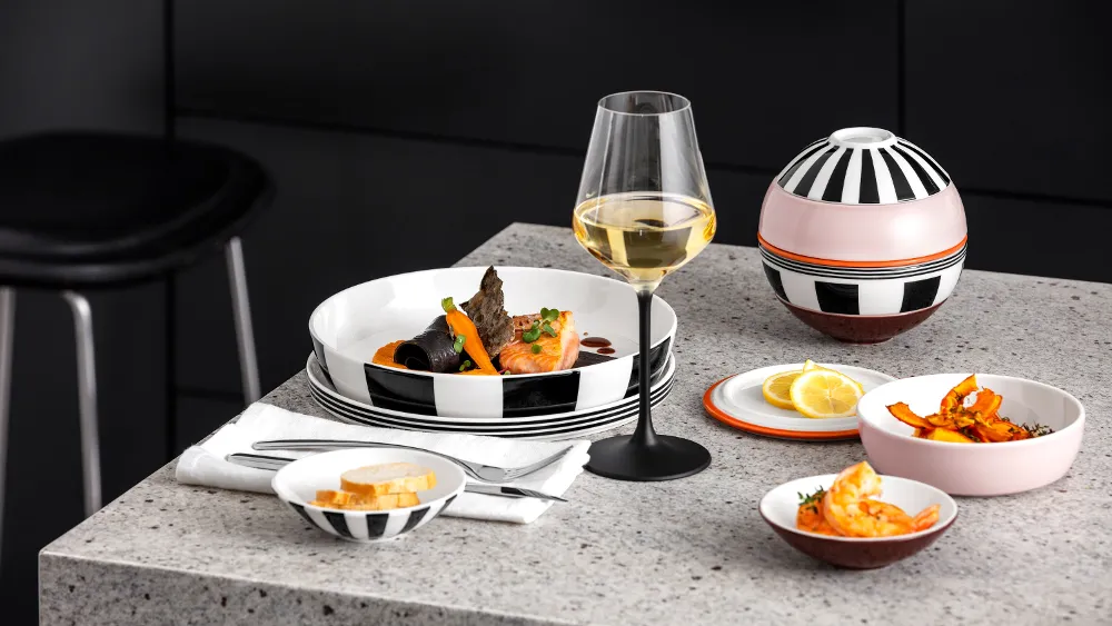 Una tavola imbandita in modo moderno con un bicchiere di vino bianco, frutti di mare serviti, pane affettato e spicchi di limone su un piano di lavoro in granito.