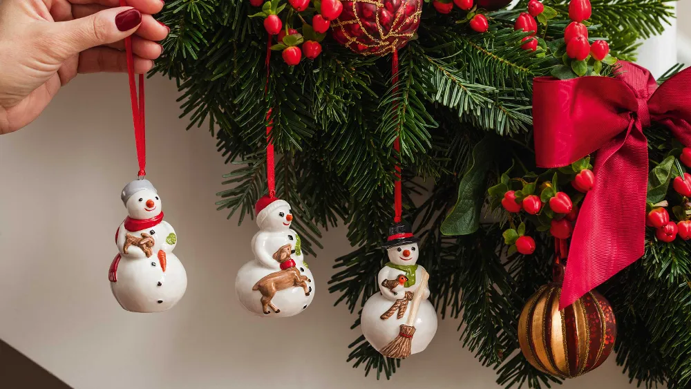 Nostalgic Ornaments Snowman ornaments are hung by hand on a decorated Christmas tree with red ribbons, berries and baubles.