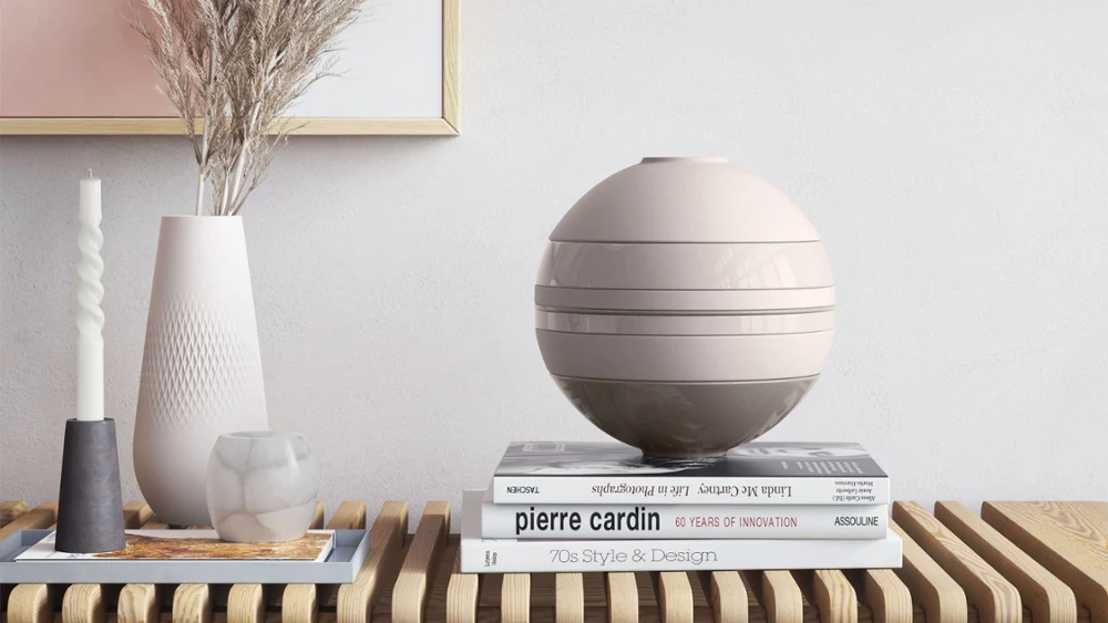 A beige La Boule from Villeroy & Boch on a wooden table next to a Manufacture vase and books.