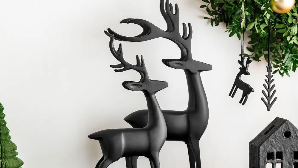 Deux rennes Black Xmas noirs sur une console noire, au-dessus de laquelle est suspendue une couronne verte avec des ornements noirs.