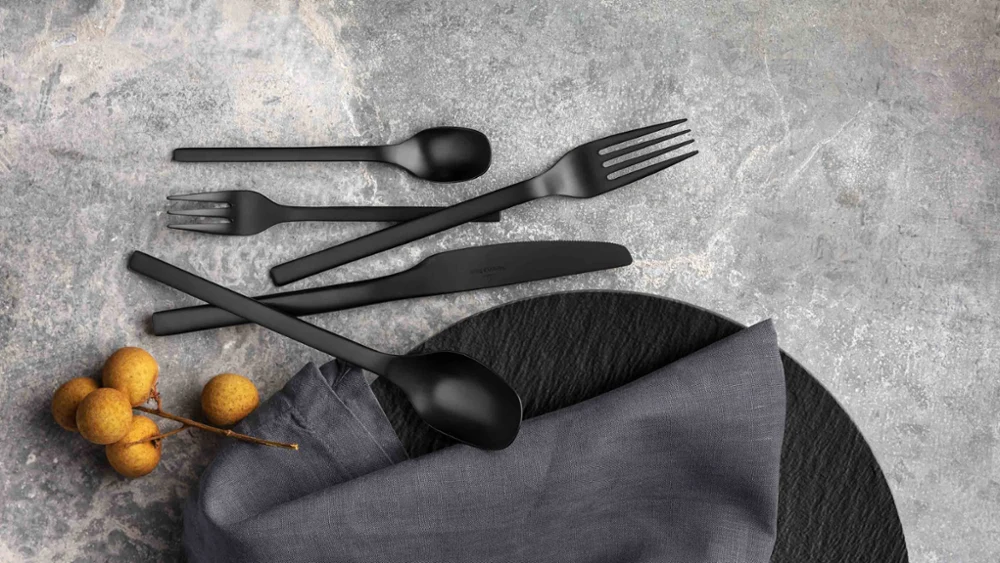 Zwarte Manufacture bestekset met stoffen servet en decoratieve bessen op een grijs gestructureerd oppervlak.