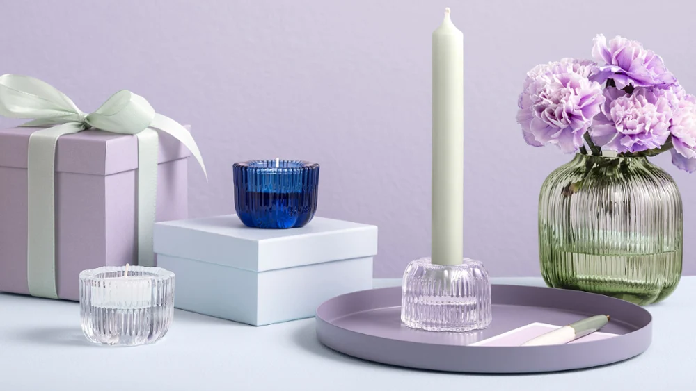 The Villeroy & Boch Fleur Vert vase with purple flowers is displayed on a surface next to gift boxes and Fleur candle holders.