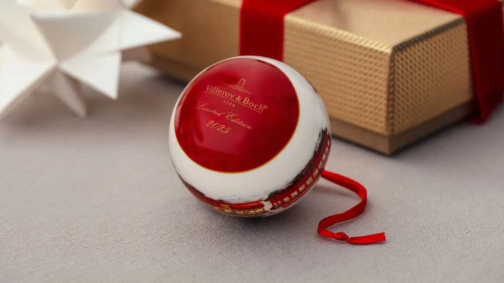 Red and white Christmas ornaments with the text "Villeroy & Boch" next to a wrapped gift and a white paper star. 