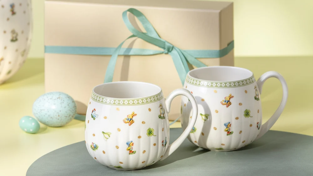Two Easter Delight mugs with floral patterns are placed in front of a gift box tied with a light blue ribbon.