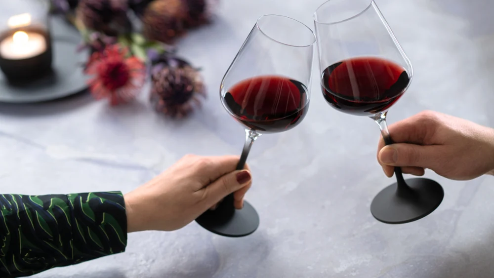 Twee mensen proosten met twee gevulde Manufacture rode wijnglazen met zwarte steel van Villeroy & Boch.