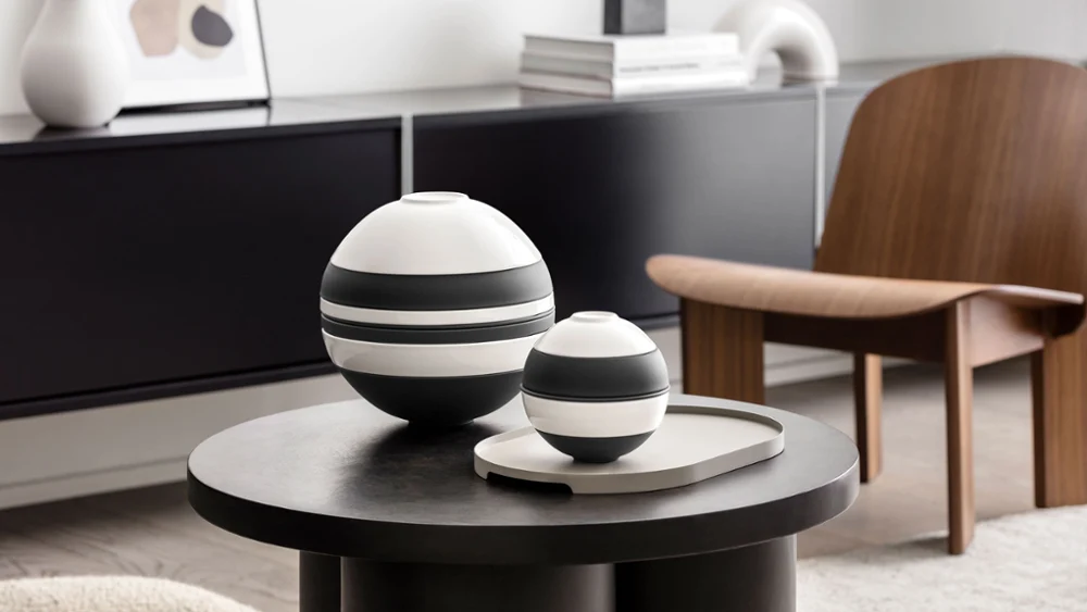 Een moderne woonkamer met een zwart-witte La Boule van Villeroy & Boch naast de zwart-witte La petite Boule op een donkere ronde tafel. 