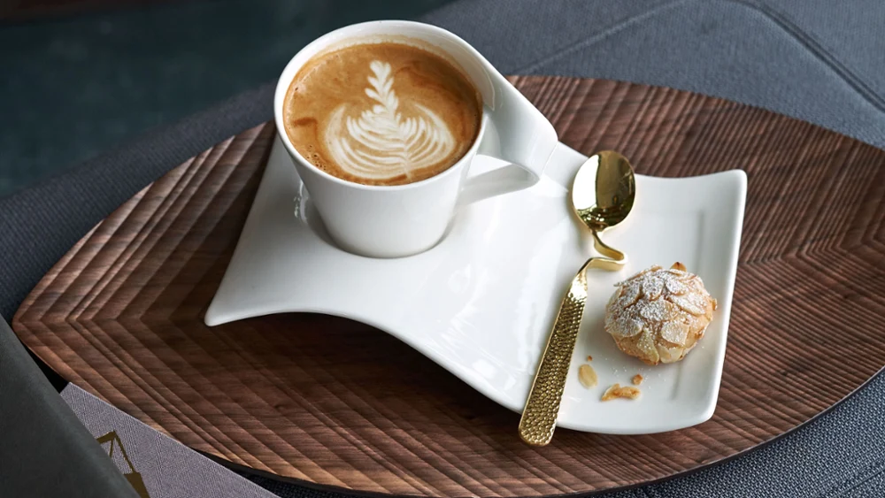 Een NewWave beker met latte art en koekjes op een houten tafel, vergezeld van een verfijnde NewWave lepel.
