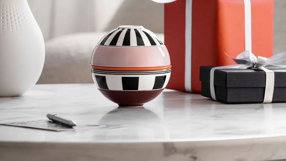 La petite Boule Memphis de Villeroy & Boch et deux cadeaux emballés sont posés sur une table en marbre, avec un vase de fleurs en arrière-plan.