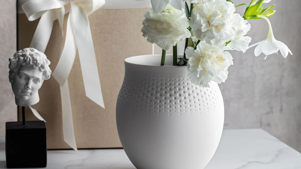 Eine großzügige Manufacture Collier Blanc Perle Vase mit feiner Punktstruktur, verpacktes Geschenk dahinter, ideal für üppige Blumenarrangements.