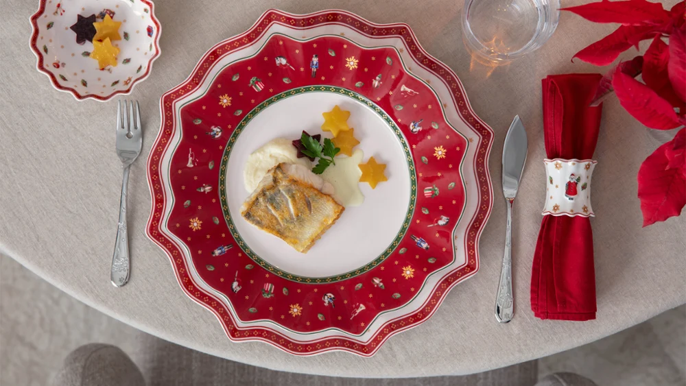 A decorative festive plate featuring fish, sauce, parsley and star-shaped vegetables on a festively laid table.