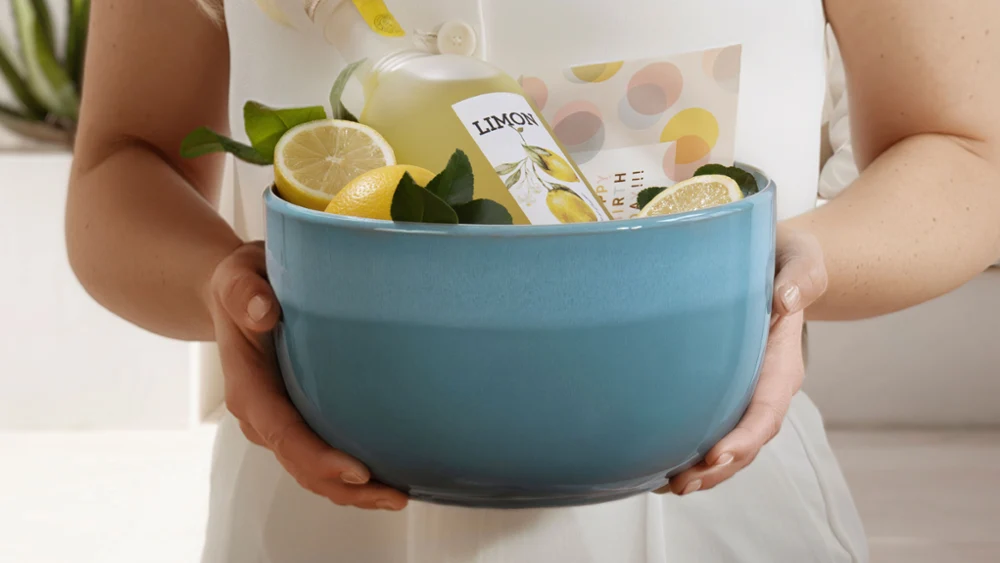 A person is holding a blue bowl from the Perlemor Aqua collection with a bottle of lemonade. A person is holding a blue bowl from the Perlemor Aqua collection with a bottle of lemonade, lemon slices and green leaves.