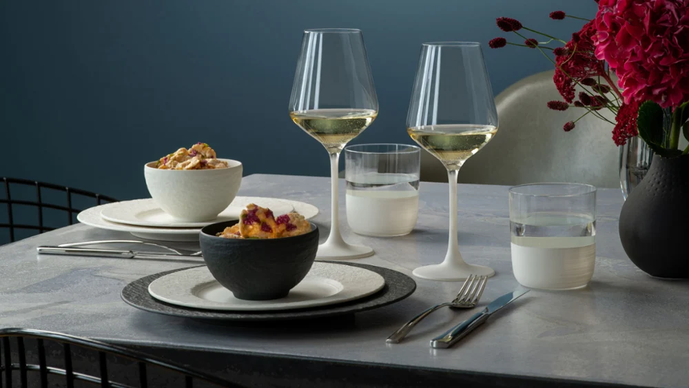 Elegant diner met twee witte wijnglazen, netjes gerangschikte borden en schalen van Manufacture met borden op een moderne tafel.