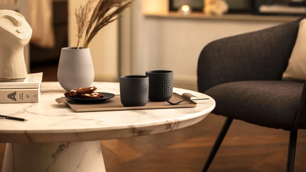Przytulny kącik w pokoju z przedmiotami dekoracyjnymi Manufacture Przytulny kącik pokoju z marmurowym stolikiem z dwoma kubkami do kawy i wazonem z kolekcji Manufacture firmy Villeroy & Boch oraz wygodnym krzesłem obok.